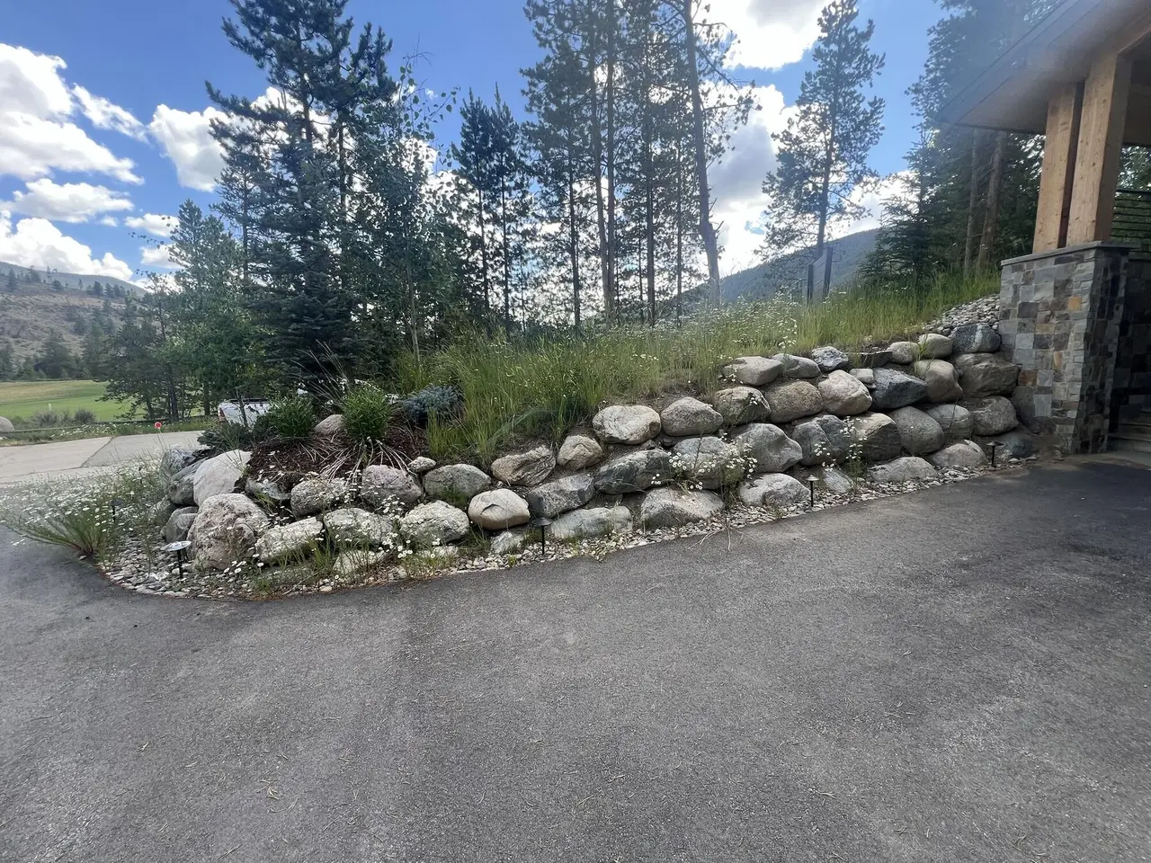 A curved boulder wall holding back a grassy slope along a driveway