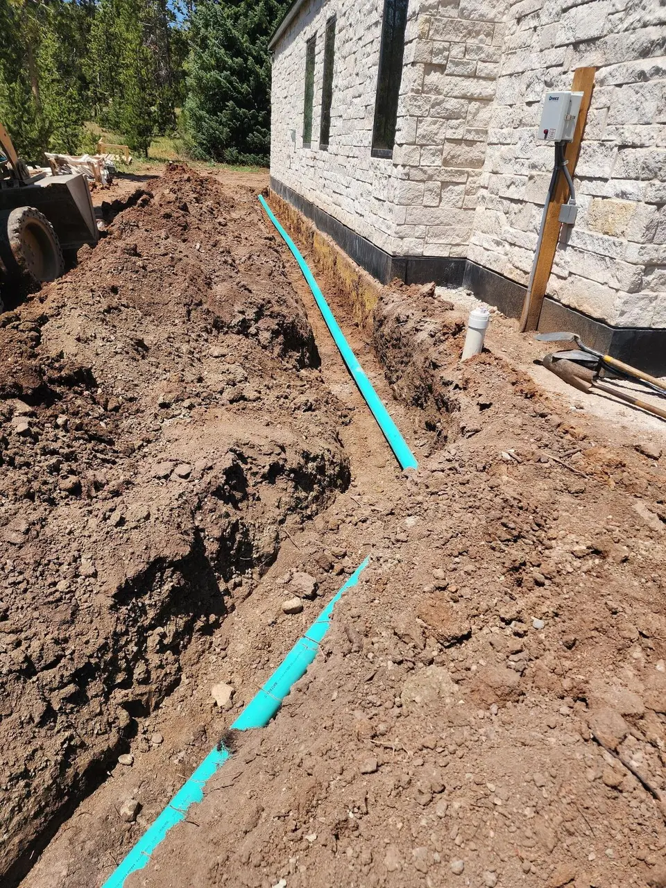 A drain line laid in a trench along the stone wall of a house