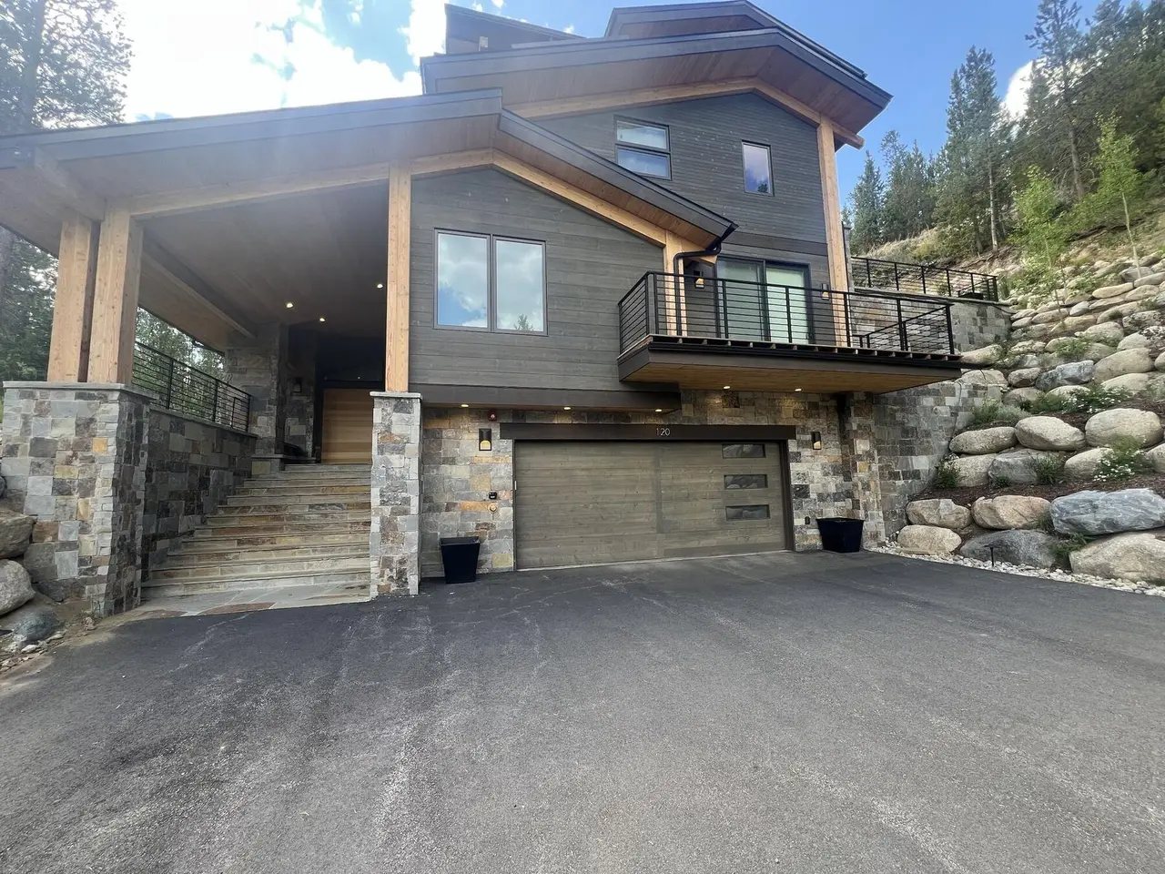 A finished mountain home with stone columns, stone stairs, and boulder walls beside the garage