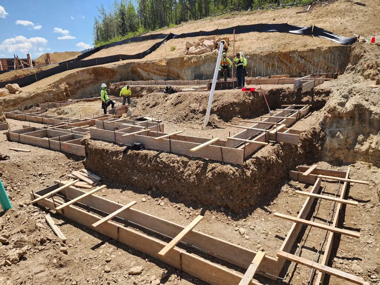 The crew setting wooden footing forms with rebar in a stepped foundation dig