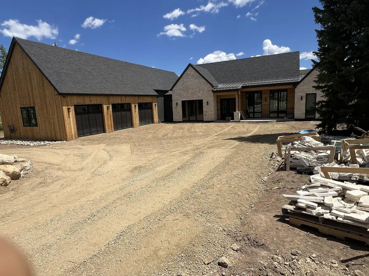 A freshly graded gravel driveway in front of a new cedar and stone home