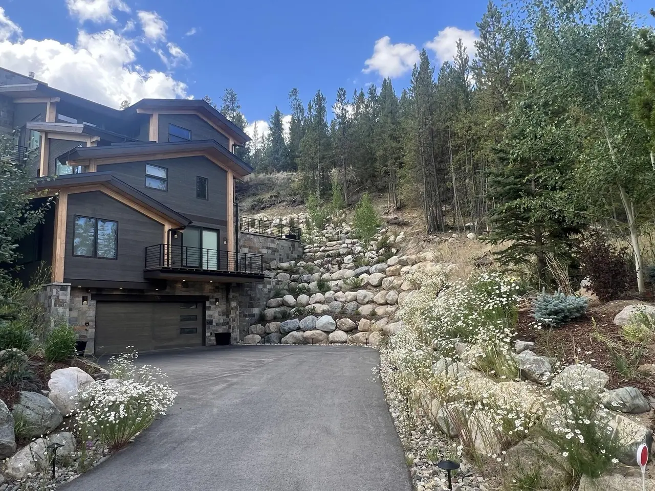 Boulder walls and wildflower beds lining a paved driveway up to a home