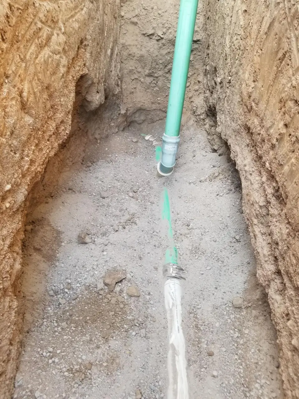 A green sewer pipe joined to a fitting at the bottom of a trench