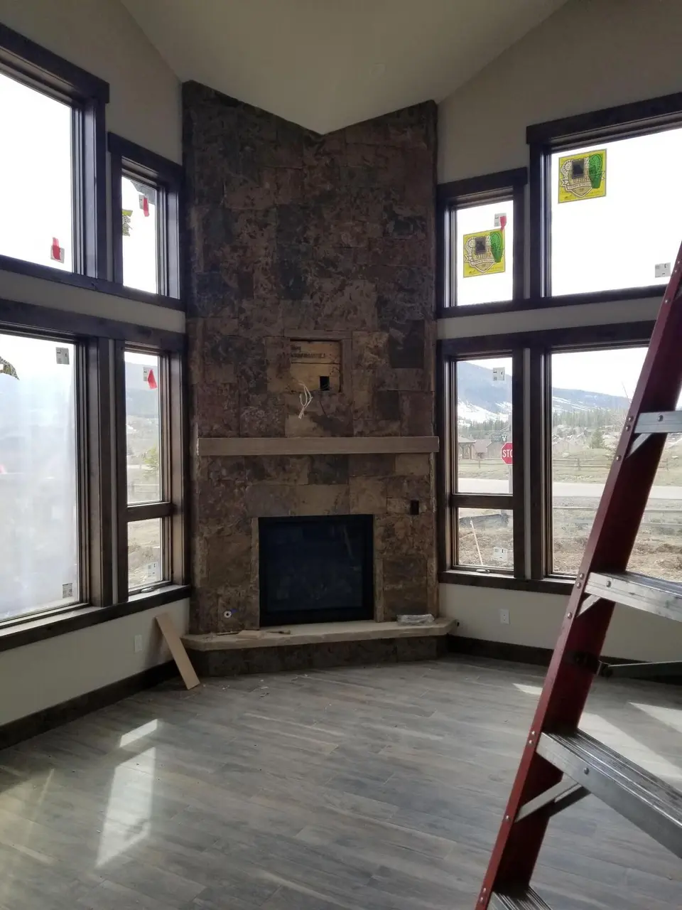 A dark stone corner fireplace rising to a vaulted ceiling between tall windows